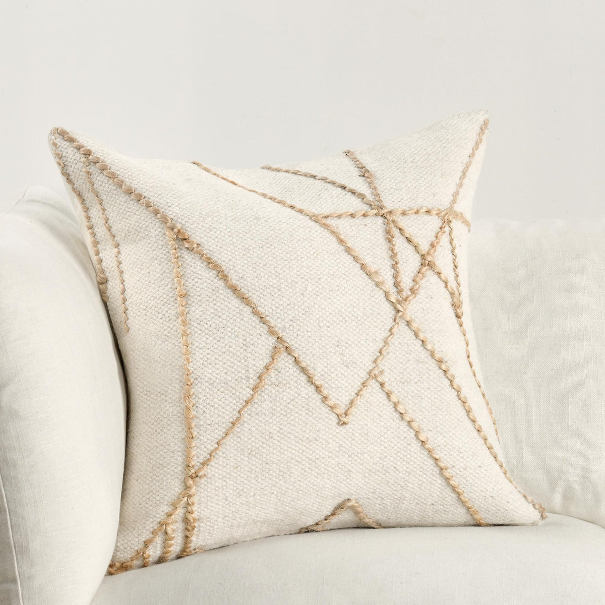 Ivory decorative pillow on sofa, natural tan embroidered geometric line pattern