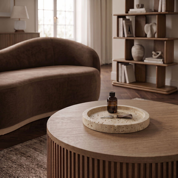 Beige travertine round tray on a table with a small bottle and dish.