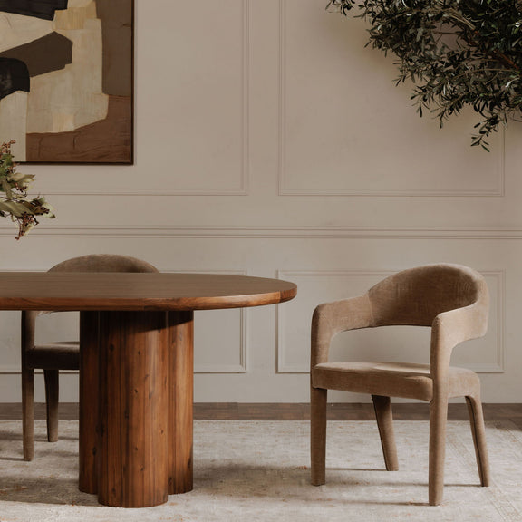 Camel upholstered dining chair with curved arms and tapered legs beside a dining table