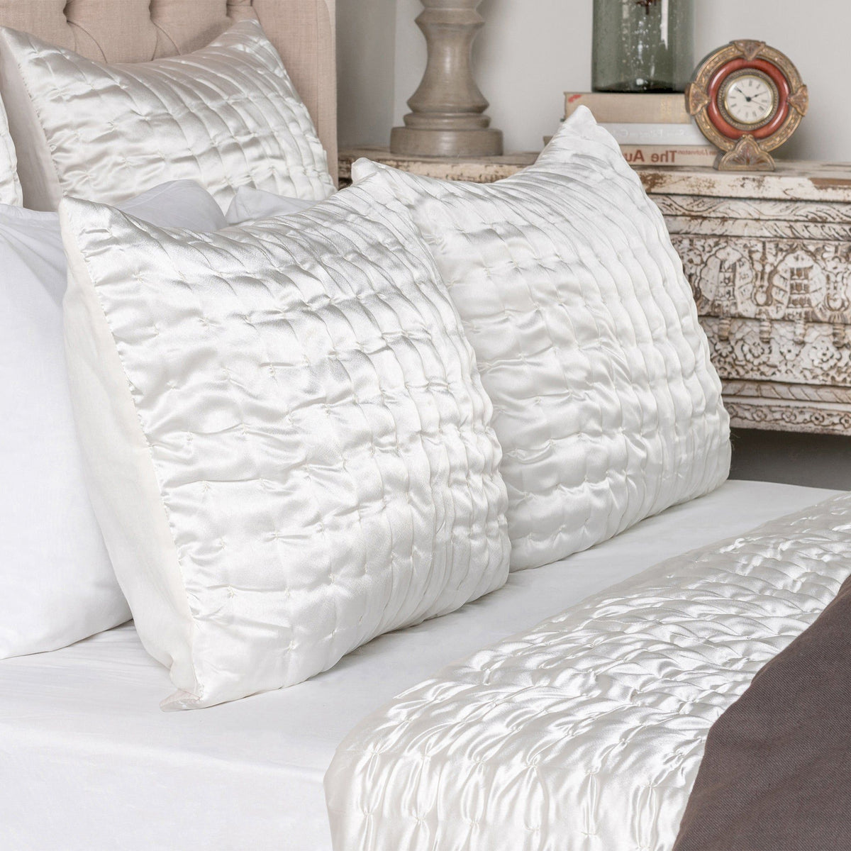 Set of white quilted decorative shams with raised crisscross stitched pattern on bed.