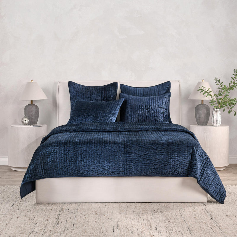 Blue velvet quilt with matching pillow shams on a white bed