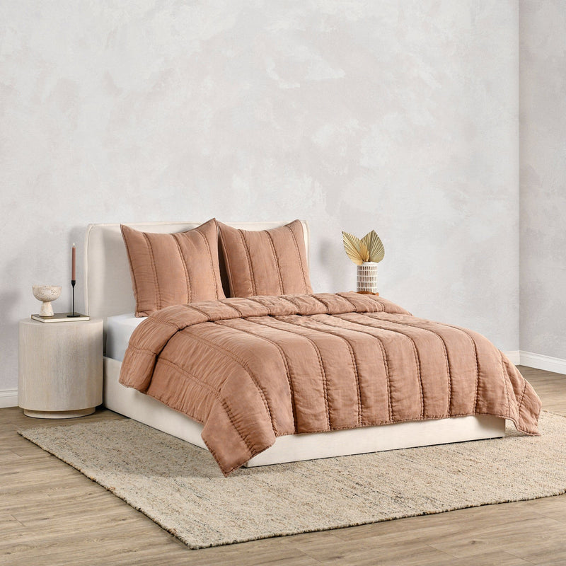 Quilt in warm clay draped over bed with matching channel quilting