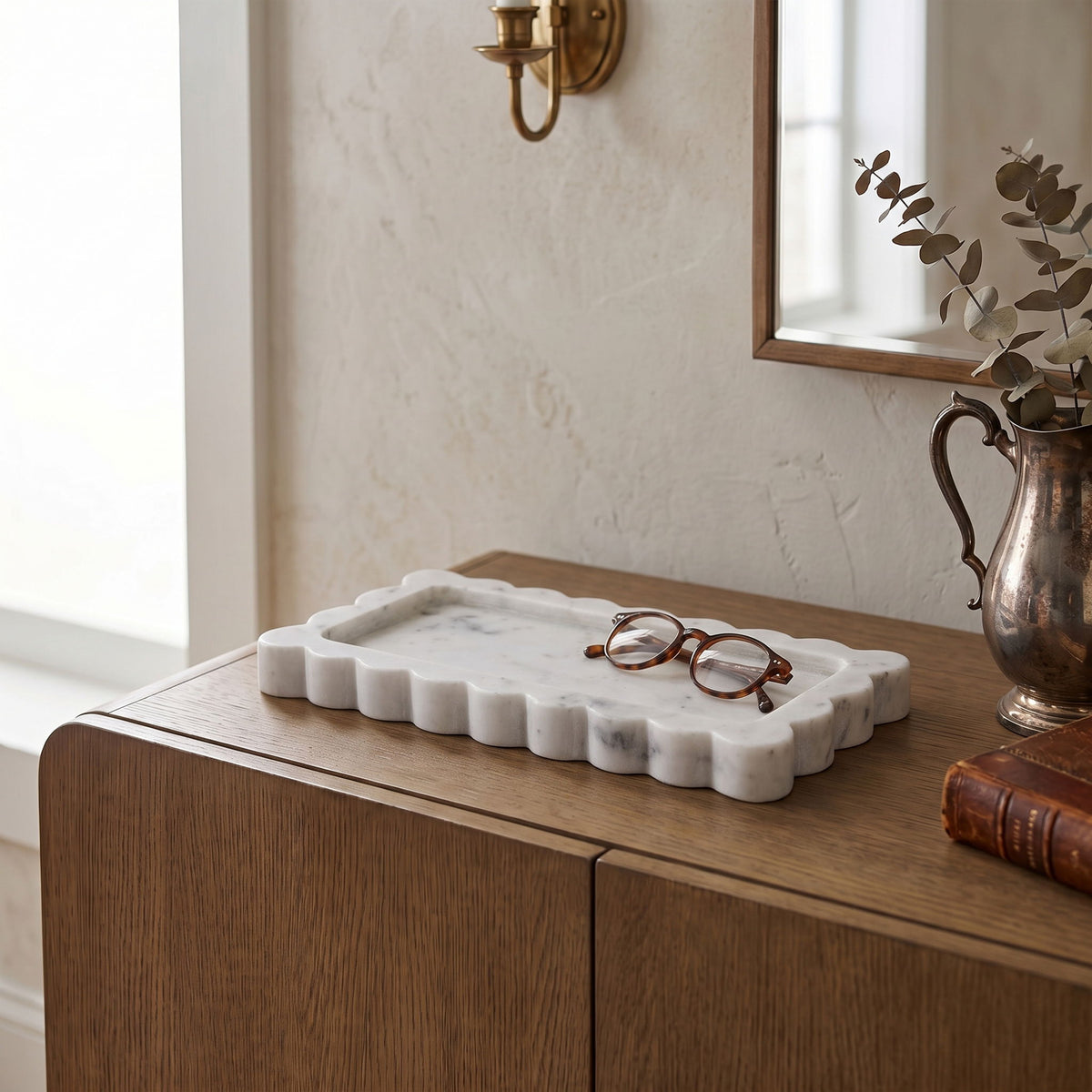 White marble tray with scalloped edge, shown on wooden table next to glasses.