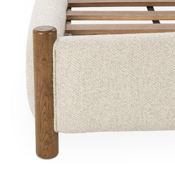 Beige upholstered bed side rail with textured fabric and dark wood foot