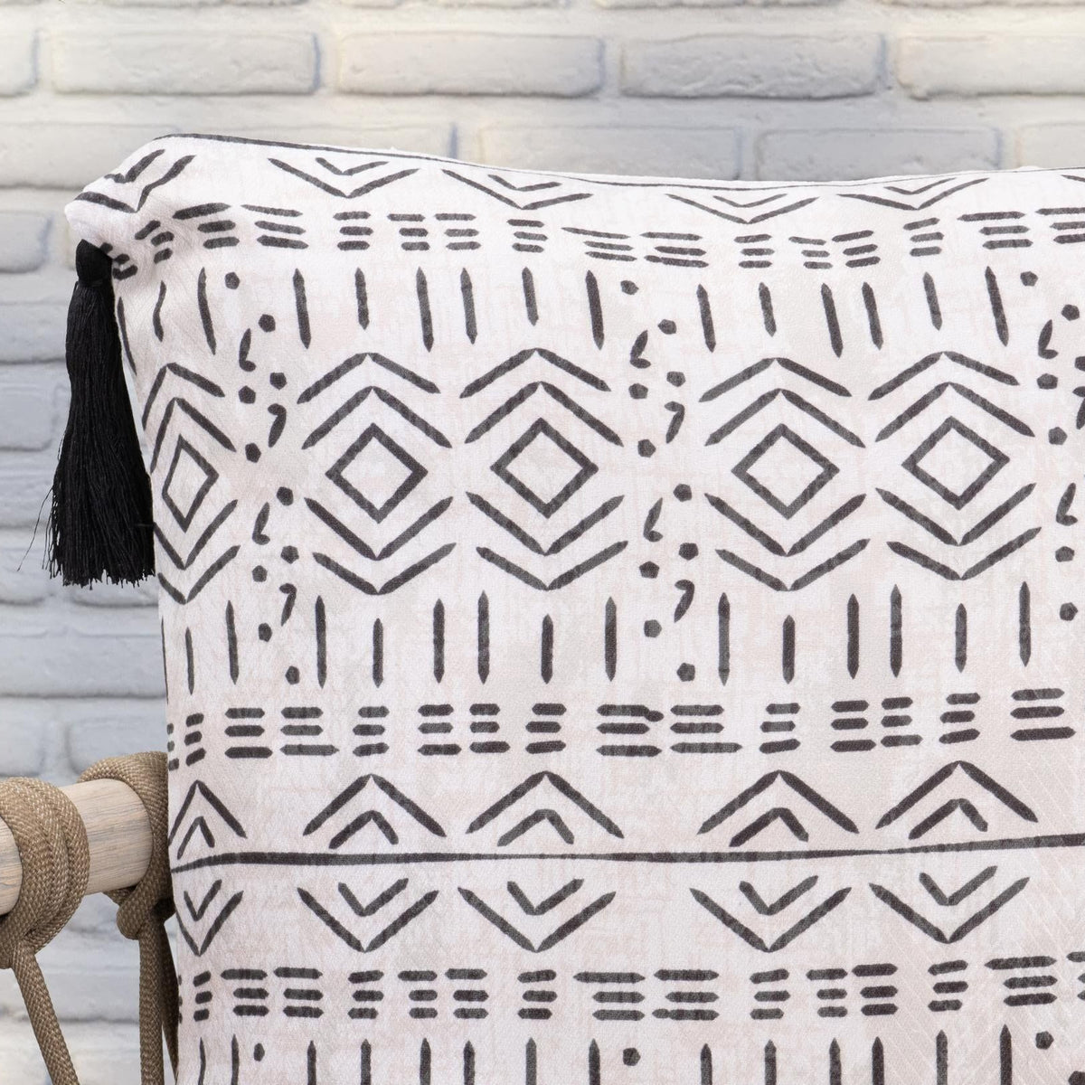 Close-up of natural pillow fabric with black geometric design and tassel fringe.