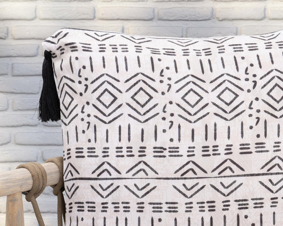 Close-up of natural pillow fabric with black geometric design and tassel fringe.