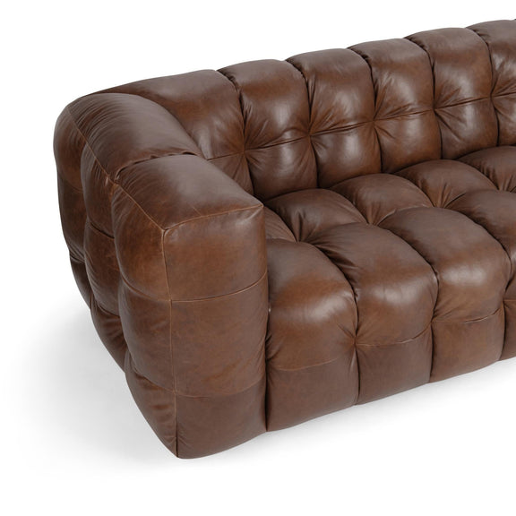 Chestnut-brown tufted leather sofa viewed at angle, with rolled arm and back.
