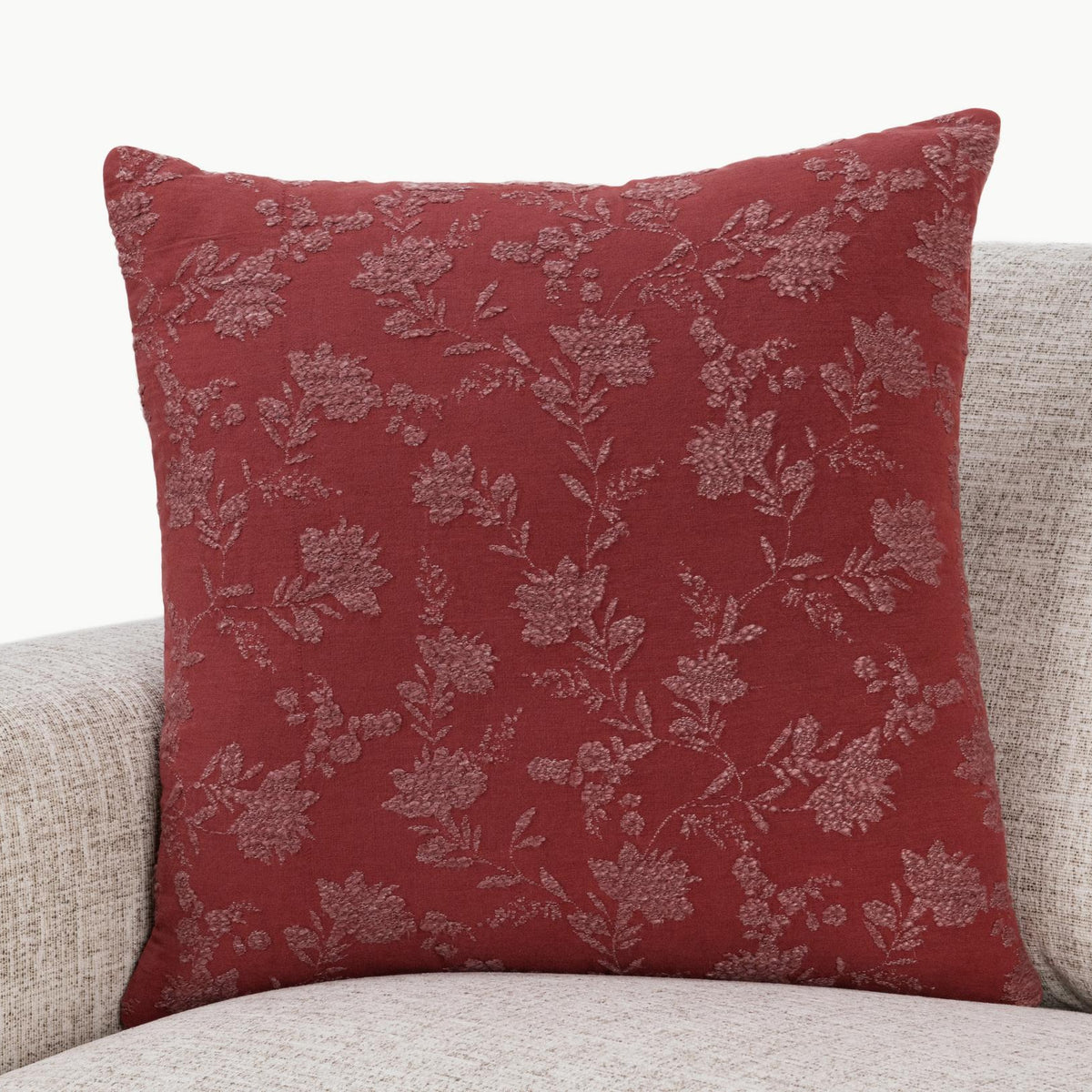 Burgundy red square pillow with light floral vine pattern, styled on a beige sofa.