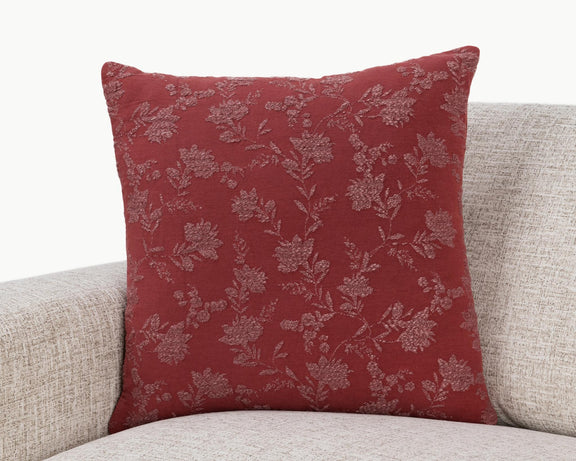 Burgundy red square pillow with light floral vine pattern, styled on a beige sofa.