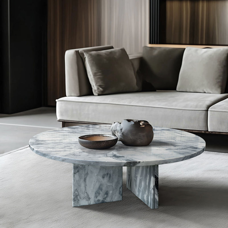 Round stone coffee table with light gray marble veining and sculpted pedestal base.