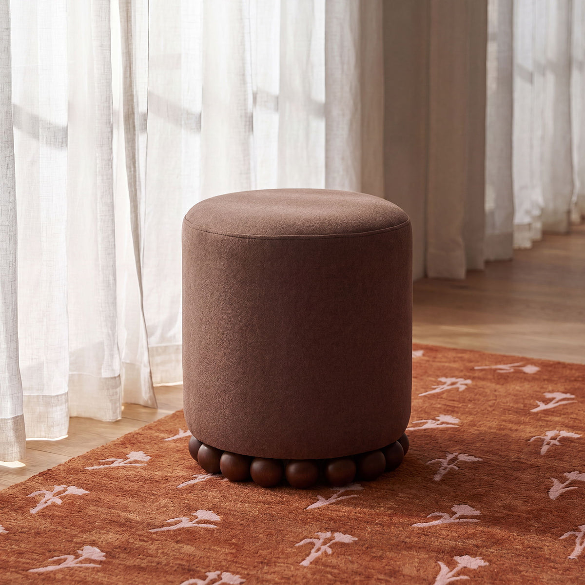 Light brown round ottoman with plush fabric and round wooden ball base