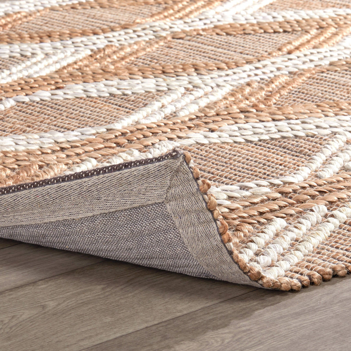 Natural fiber rug edge detail showing woven texture and gray fabric backing.