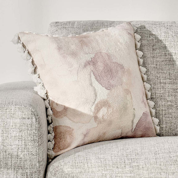 Peach floral accent pillow with white tassel fringe on sofa