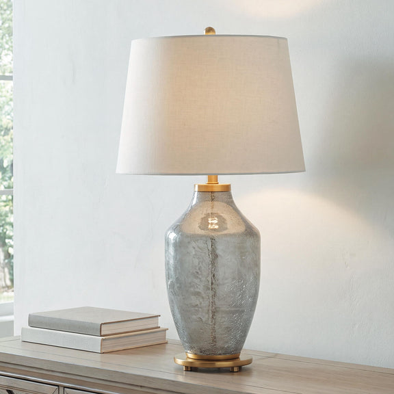 Glass table lamp with textured clear-gray body, beige fabric shade, and brass socket