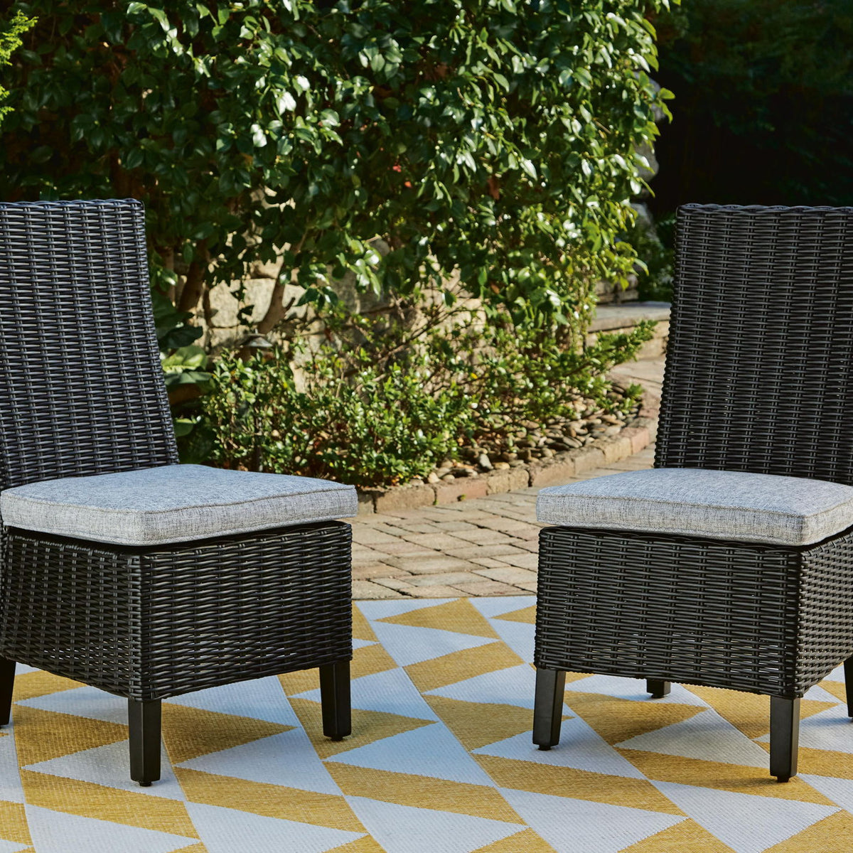 Set of 2 black woven wicker side chairs with light gray cushions outdoors