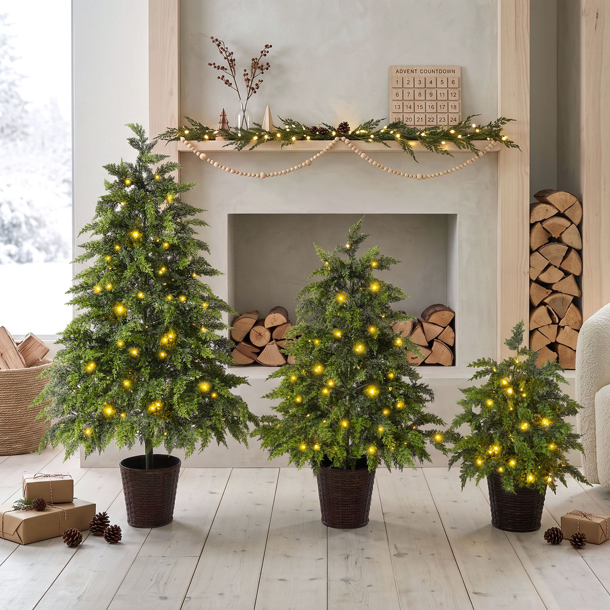Three green artificial Christmas trees with cascading branches, warm LED lights, and woven pots.