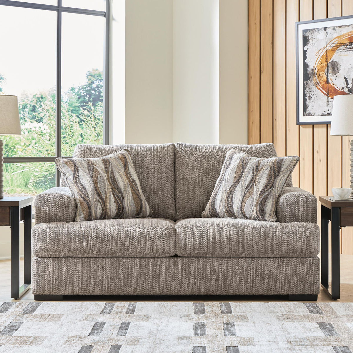 Gray loveseat sofa with striped throw pillows, black legs, and textured upholstery