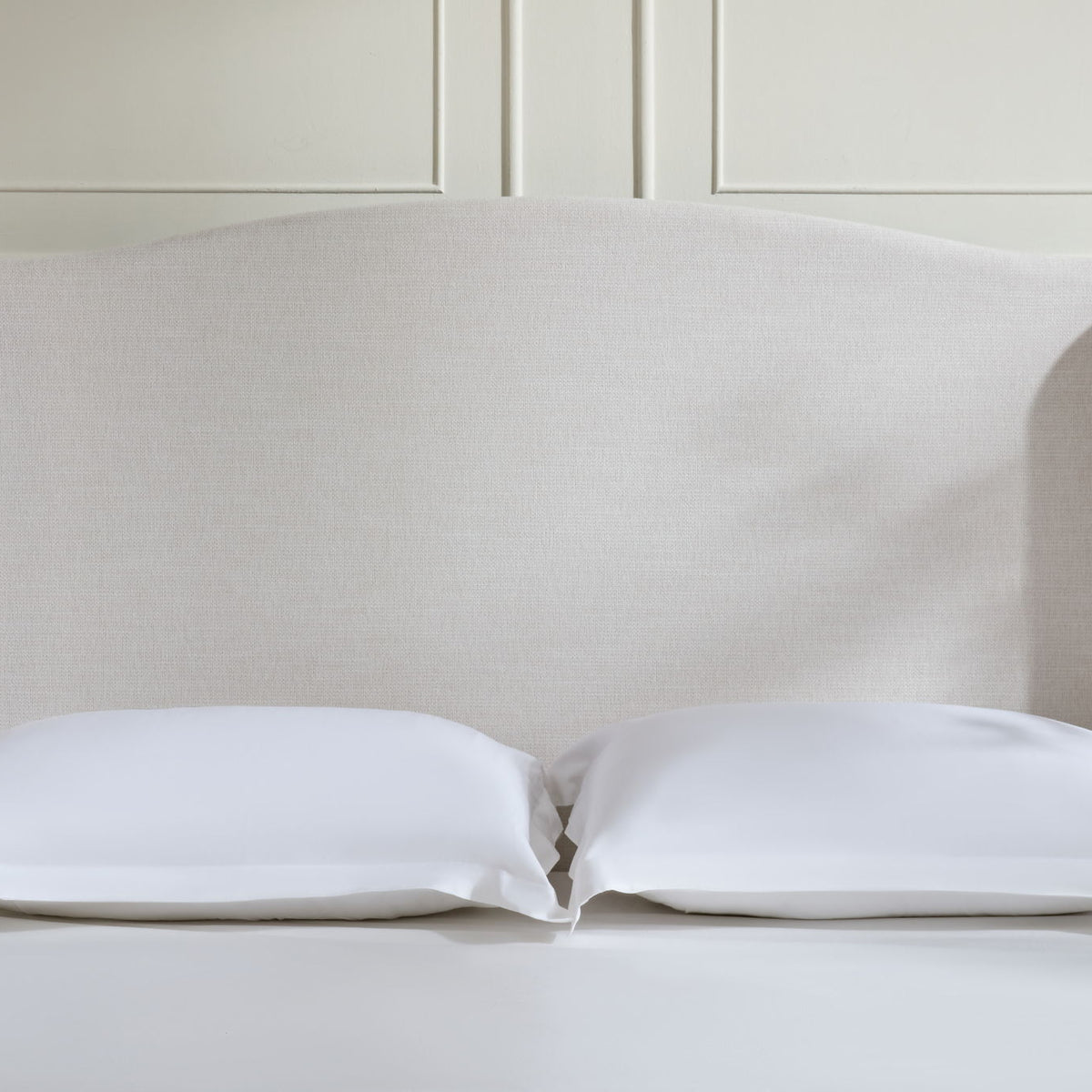 Beige upholstered headboard with two pillows on a low-profile king bed