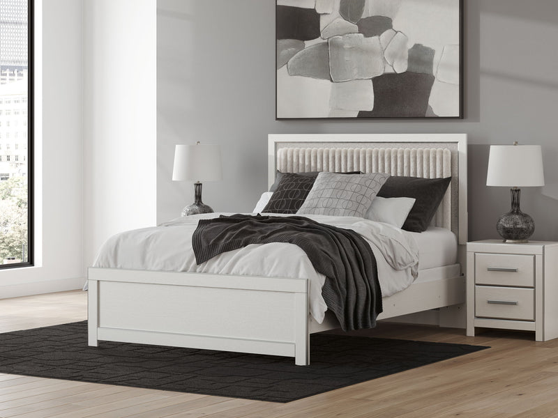 Upholstered panel bed with white frame, upholstered headboard, and layered bedding with throw blanket.