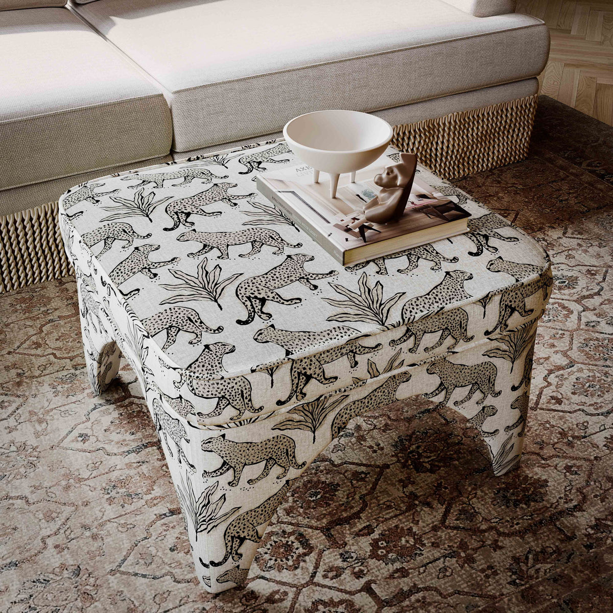 Upholstered ottoman with white jungle animal print fabric, round padded top, short turned legs