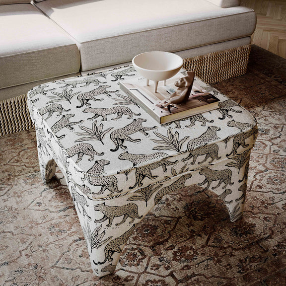 Upholstered ottoman with white jungle animal print fabric, round padded top, short turned legs