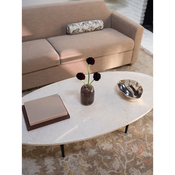 Round beige stone coffee table with dark legs, vase, book, and metal bowl on top