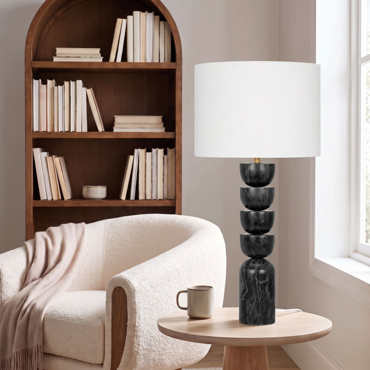 Table lamp beside sofa with white fabric drum shade and stacked dark marble base, brass accents