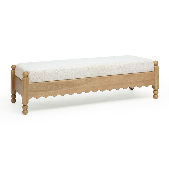 Low cream bench with textured cushion, light wood sides, scalloped apron and rounded feet.
