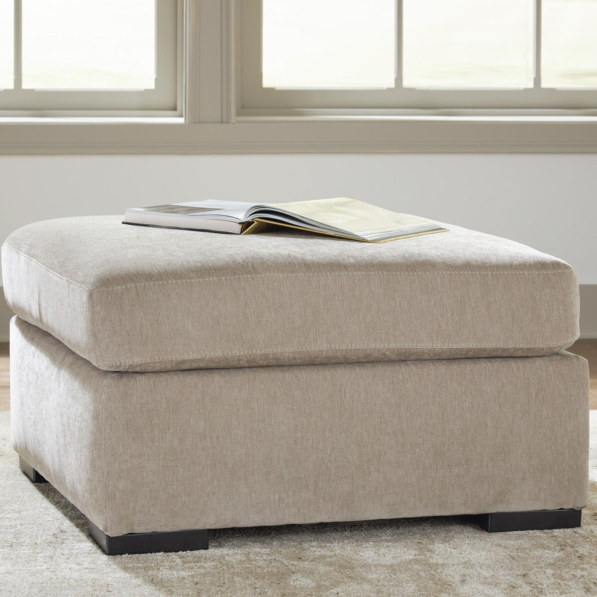 Oversized accent ottoman in light neutral fabric with black legs and open book