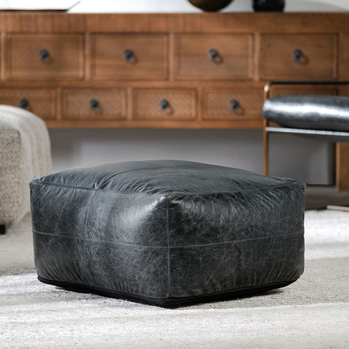 Dark leather pouf ottoman with horizontal seam and textured finish, low rounded shape