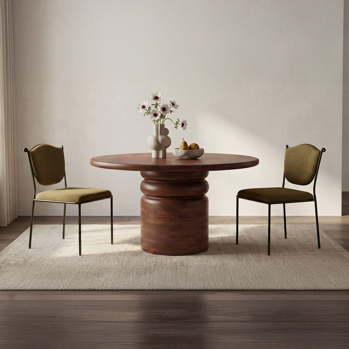 Pedestal dining table with oval wood top, styled with two upholstered chairs