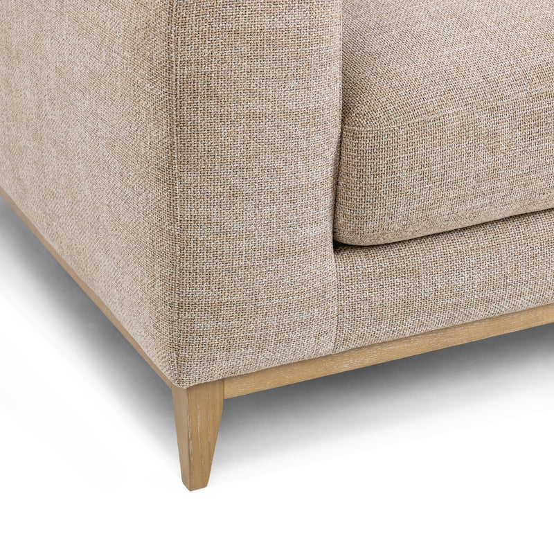 Close-up of light sand sofa fabric texture and tapered wooden legs.