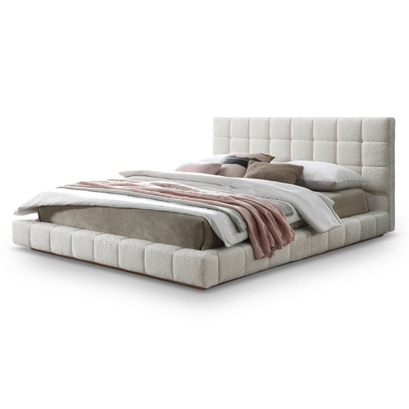 Beige upholstered bed frame with tufted headboard and draped striped blanket