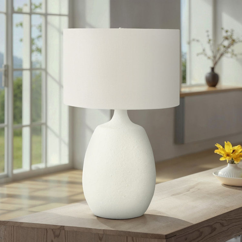 Cream resin table lamp with fabric drum shade on end table, rounded base