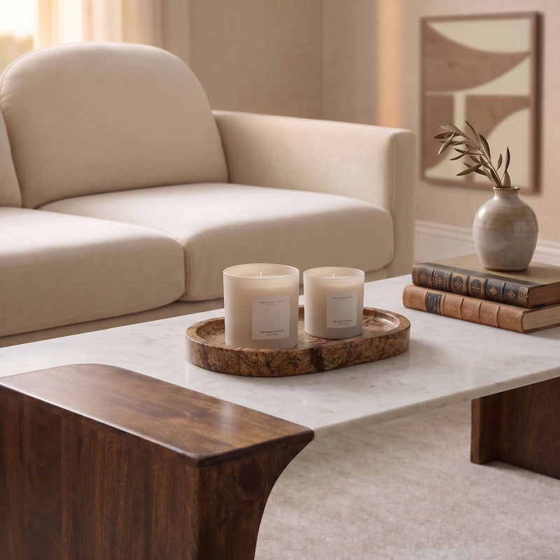 Brown marble tray holding two white candles on a table.