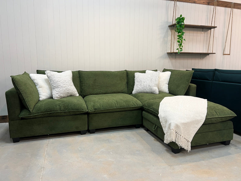 Modular sectional sofa in olive green fabric with white accent pillows and chaise
