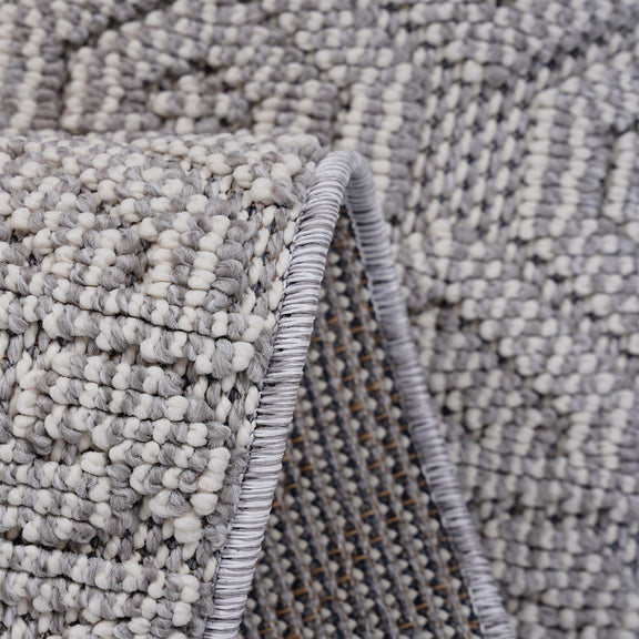 Geometric rug corner detail with braided fringe and textured dark gray pile