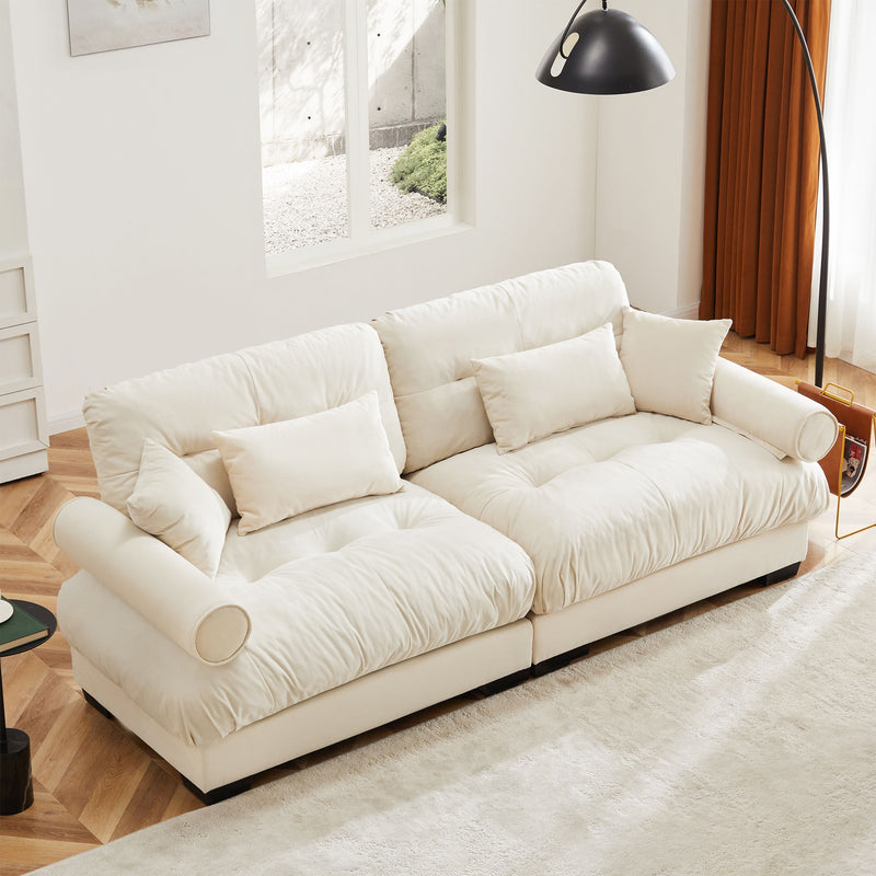 Beige upholstered sofa with tufted cushions, back throw pillows, and rounded bolster arms