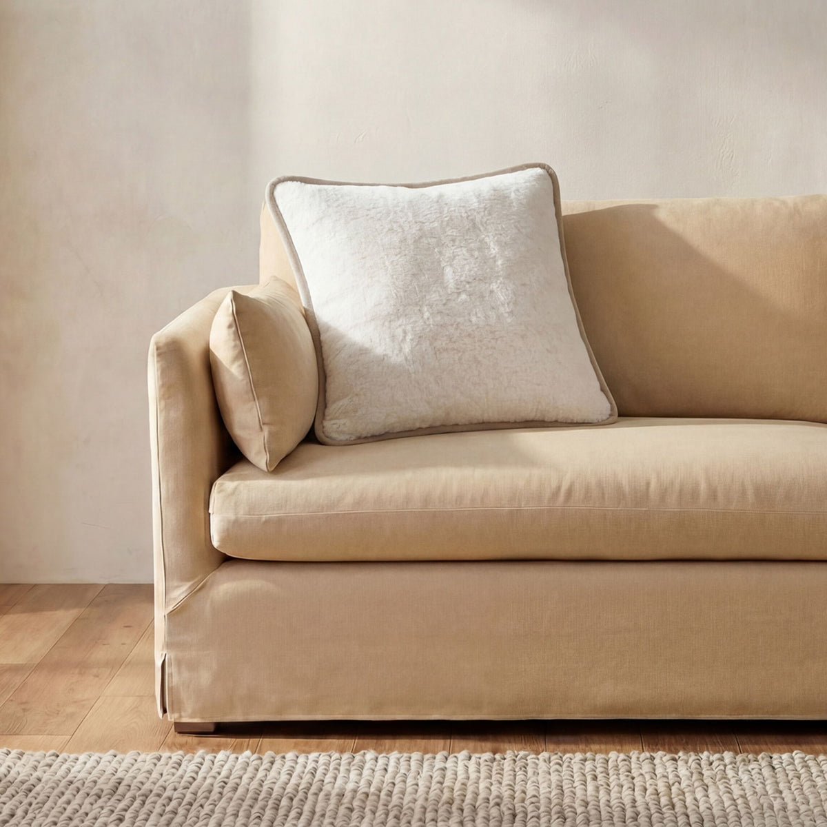 Cream faux fur cushion on beige sofa, square design with piped edge