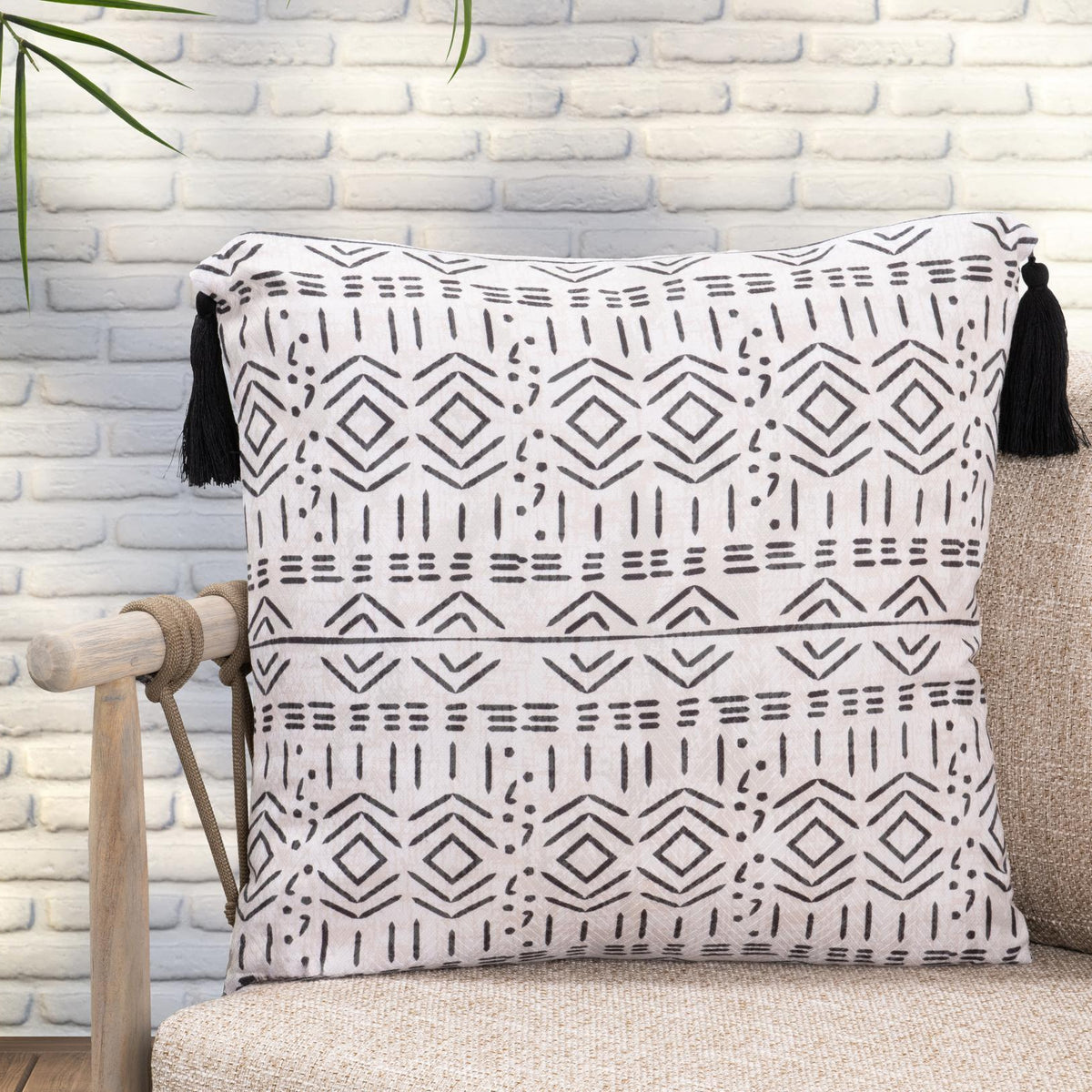 Natural geometric accent pillow with black tassels, styled on a beige sofa.