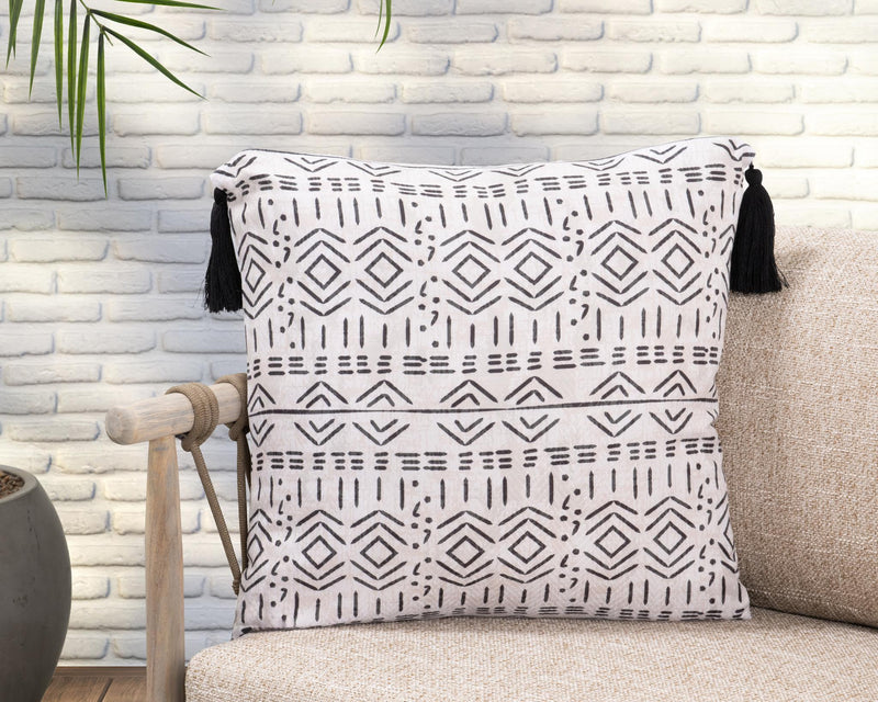 Natural geometric accent pillow with black tassels, styled on a beige sofa.