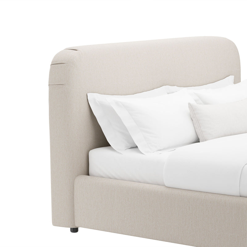 Beige rounded upholstered bed frame with curved headboard and layered white pillows