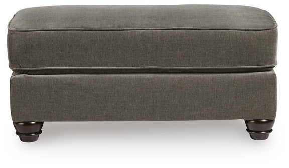 Dark gray fabric ottoman with low profile base and turned legs