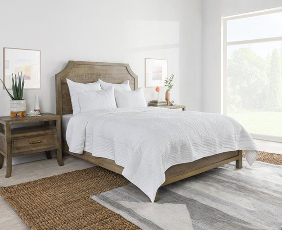 White quilted decorative shams on a bed with subtle stitched texture and piping.