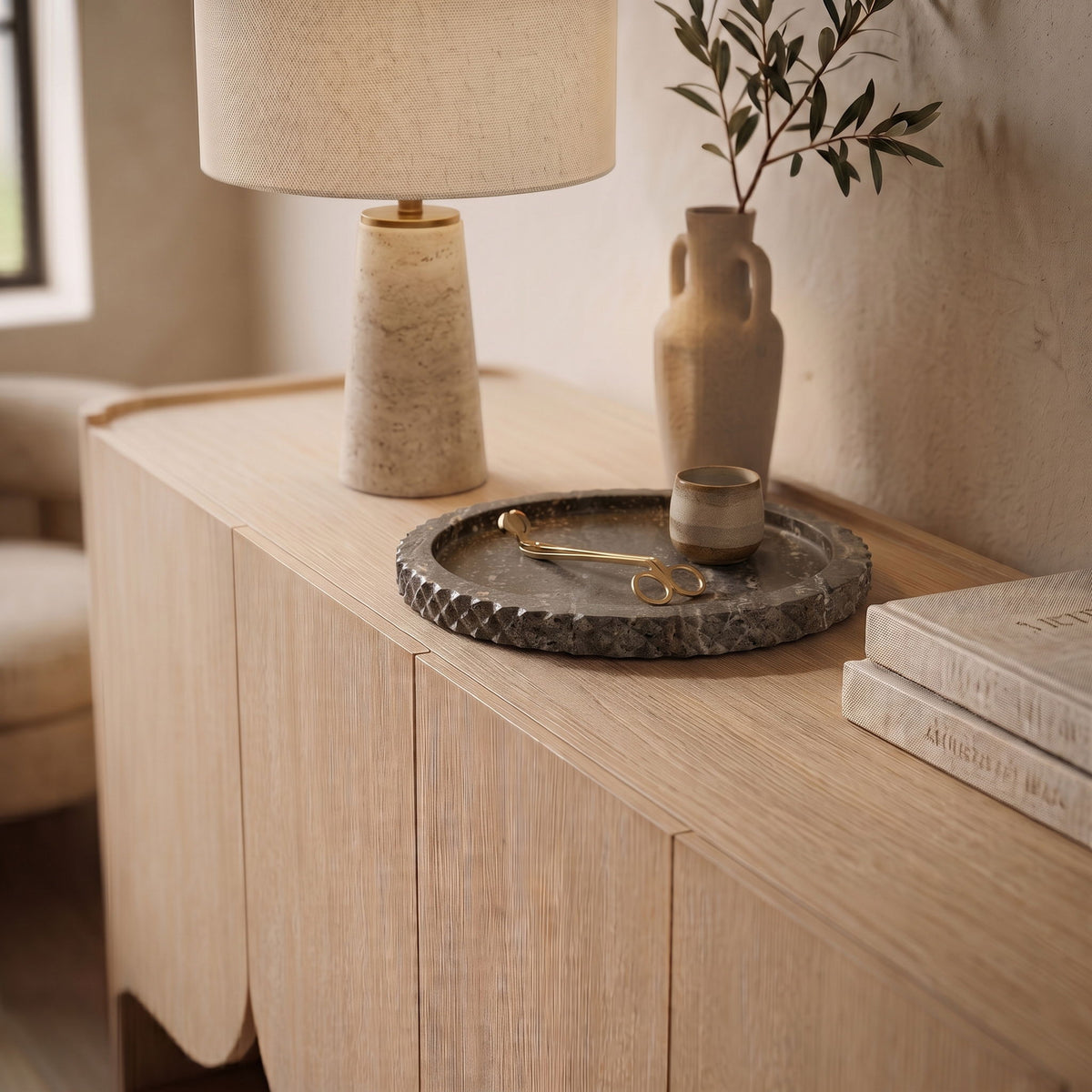 Gray travertine tray on wooden dresser holding small brass scissors and tools.