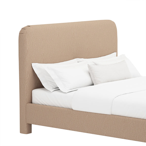 Light brown upholstered bed with rounded headboard, white sheets and stacked pillows