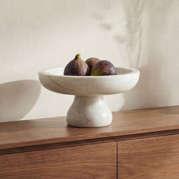 White speckled pedestal bowl filled with dark purple figs on tabletop