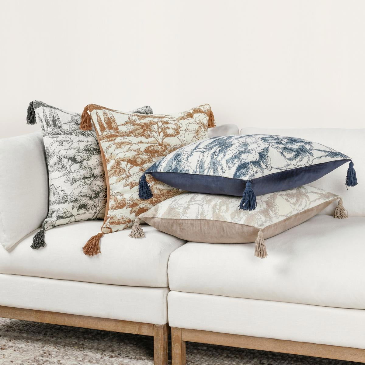 Clay forest-print throw pillow with tassels on a sofa, beige and rust-brown pattern.