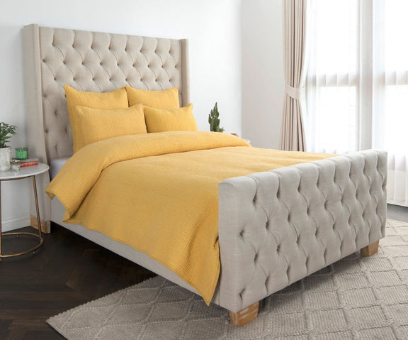 Sunflower yellow quilt set with matching pillows on a bed over a textured base.