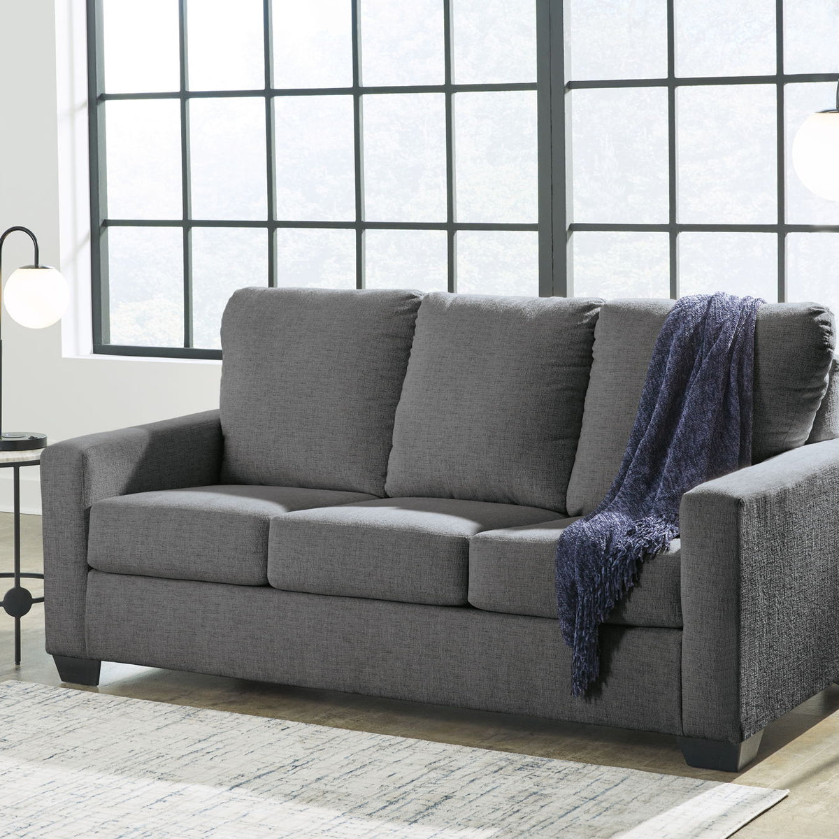 Dark gray 3-seat sofa with square arms, tufted cushions, and a blue throw blanket draped